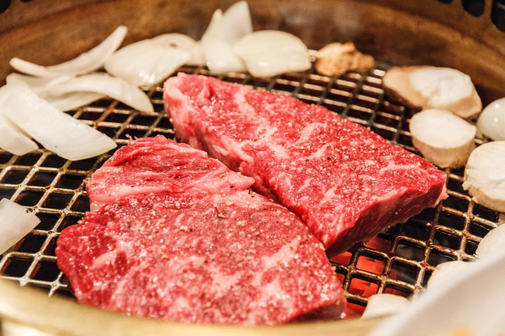 raw marbled wagyu slices grilling over charcoal flames